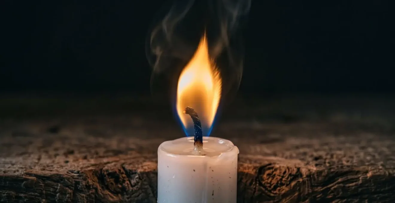 Gros plan sur une flamme de bougie blanche avec reflets dorés sur une surface en bois naturel